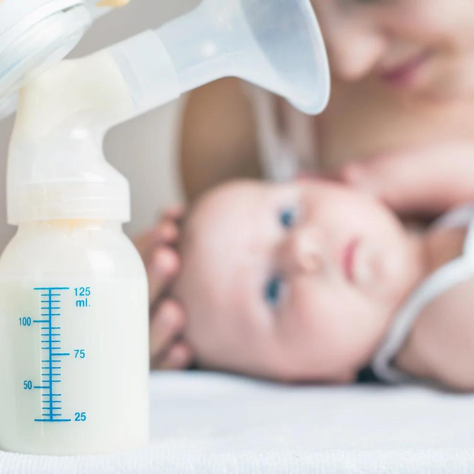 Baby in the background looking at a bottle of breast milk from a breast pump