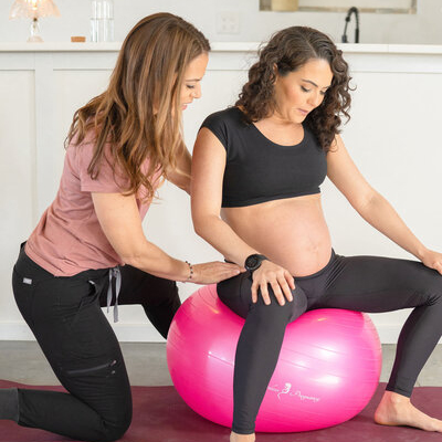 Trainer working with a pregnant woman sitting on a yoga ball