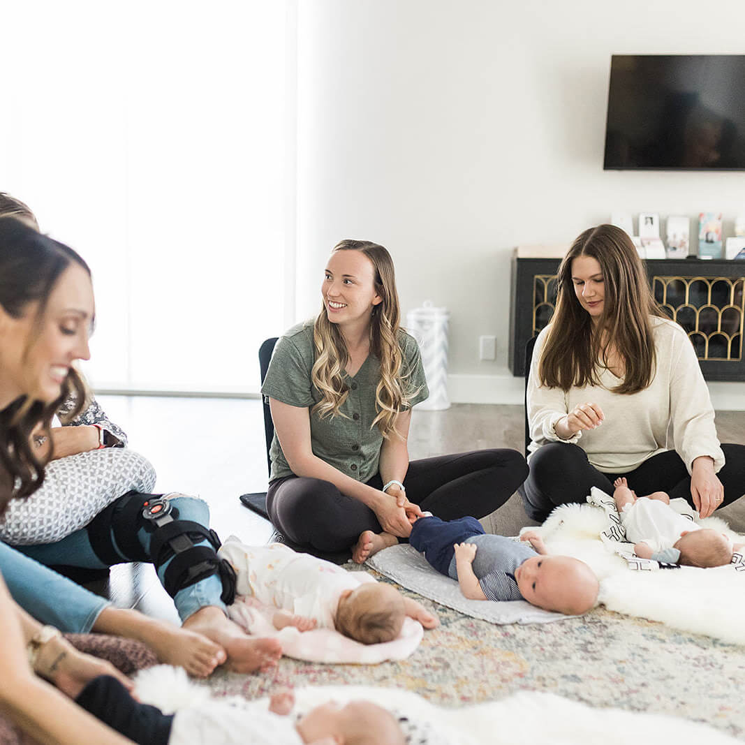 Group of smiling moms sitting with babies on blankets out in front of them on the floor