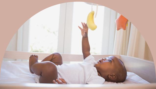 Baby laying on its back playing with a colorful mobile above its head